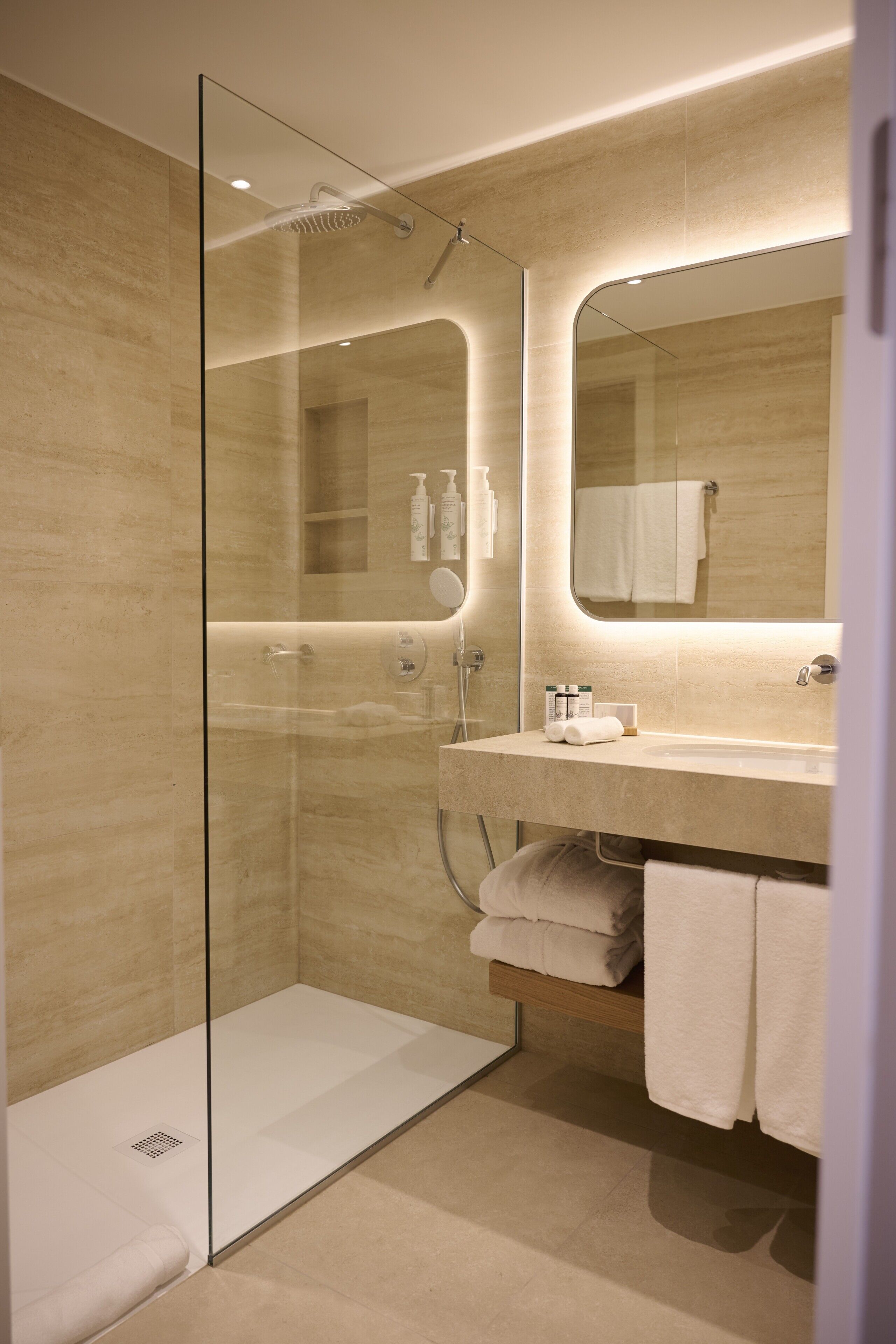 Un baño moderno con ducha envuelta en vidrio, tocador con espejo y toallas dobladas con esmero.
