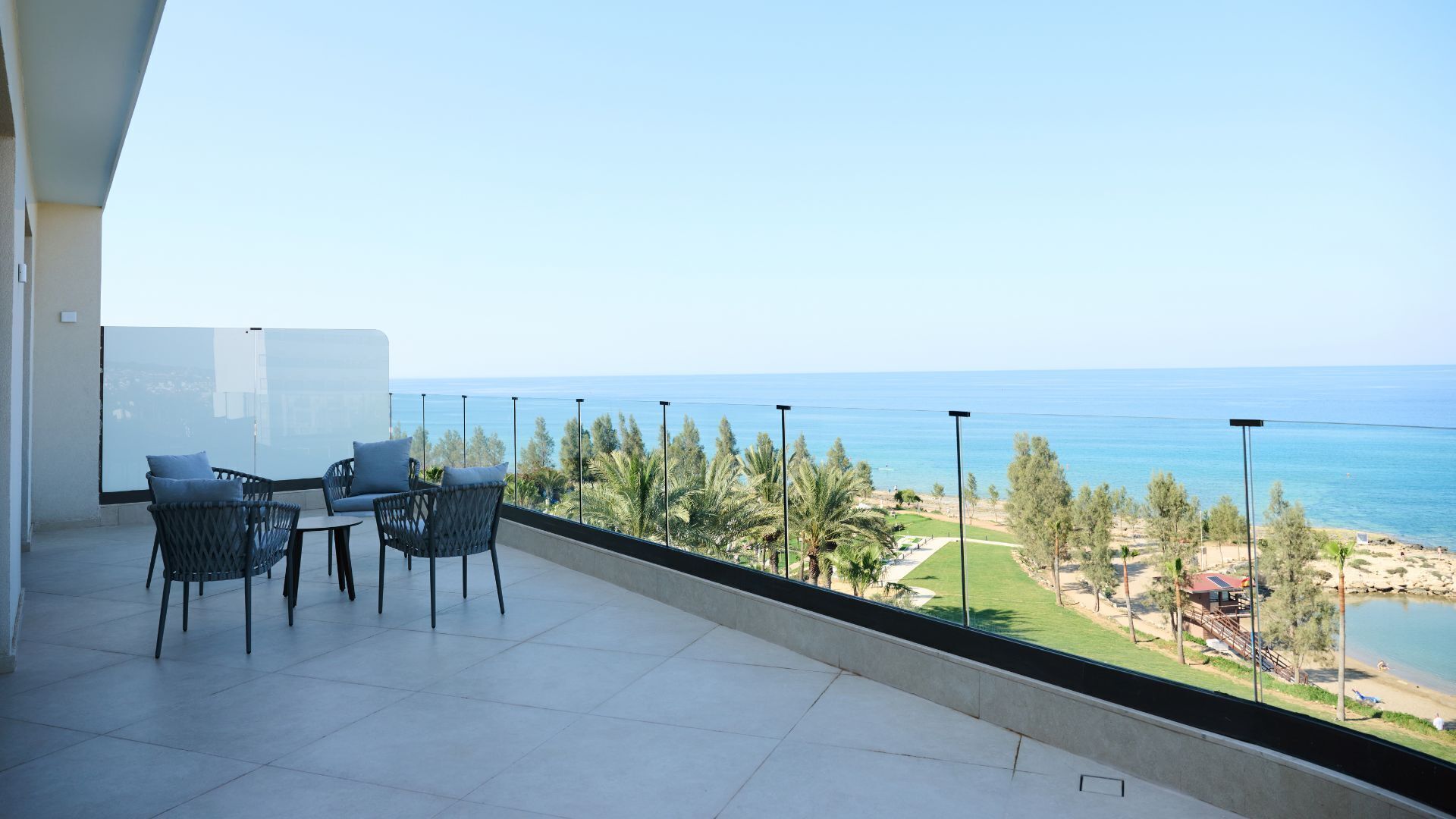 Ein Balkon mit Tisch und Stühlen, mit Blick auf einen Strand und das Meer.