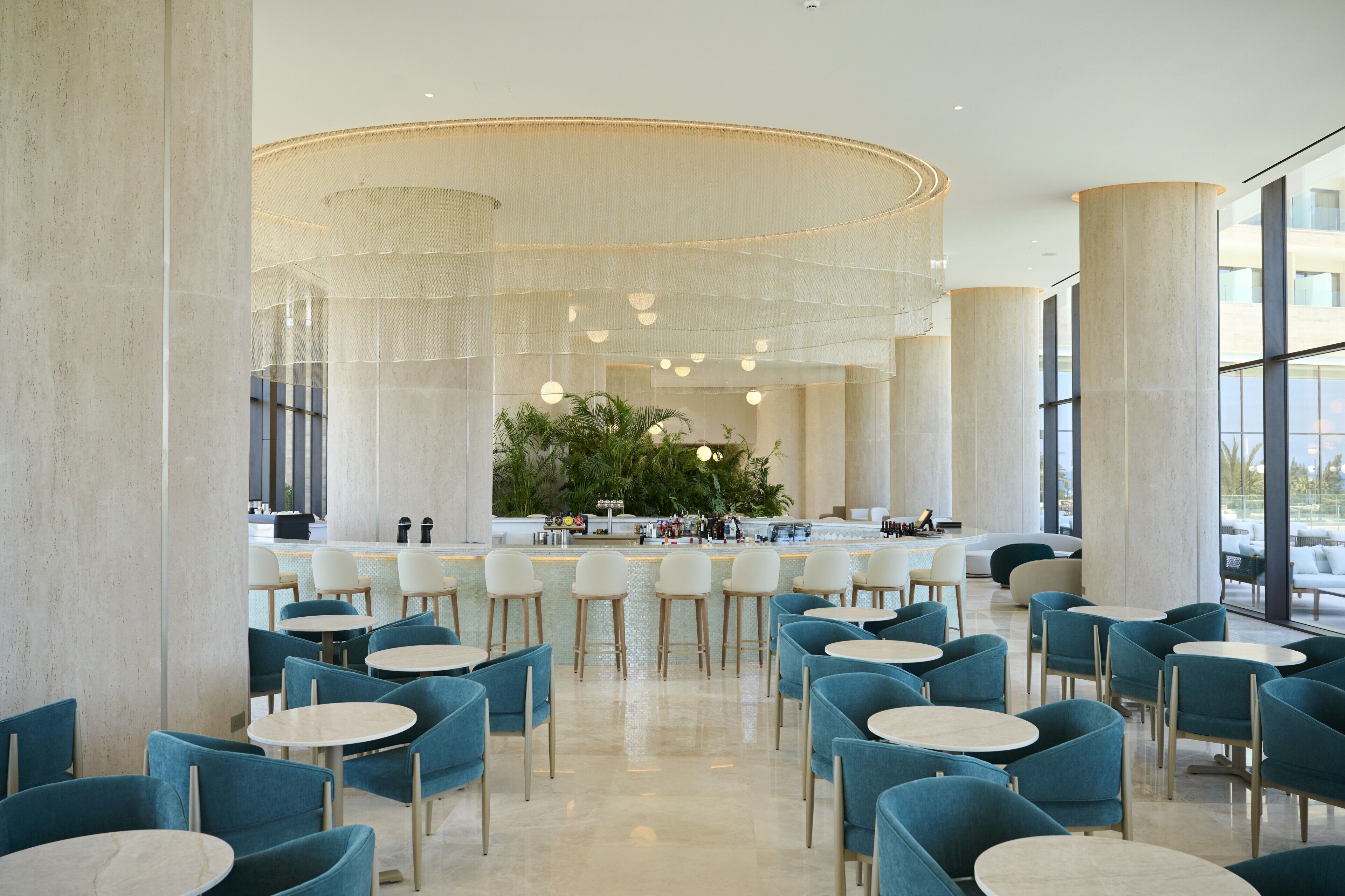 A spacious indoor area with multiple seating arrangements, a central bar area, and large windows providing natural light.