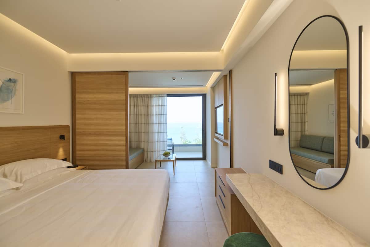 Habitación de hotel con cama, escritorio, espejo y vistas al exterior.