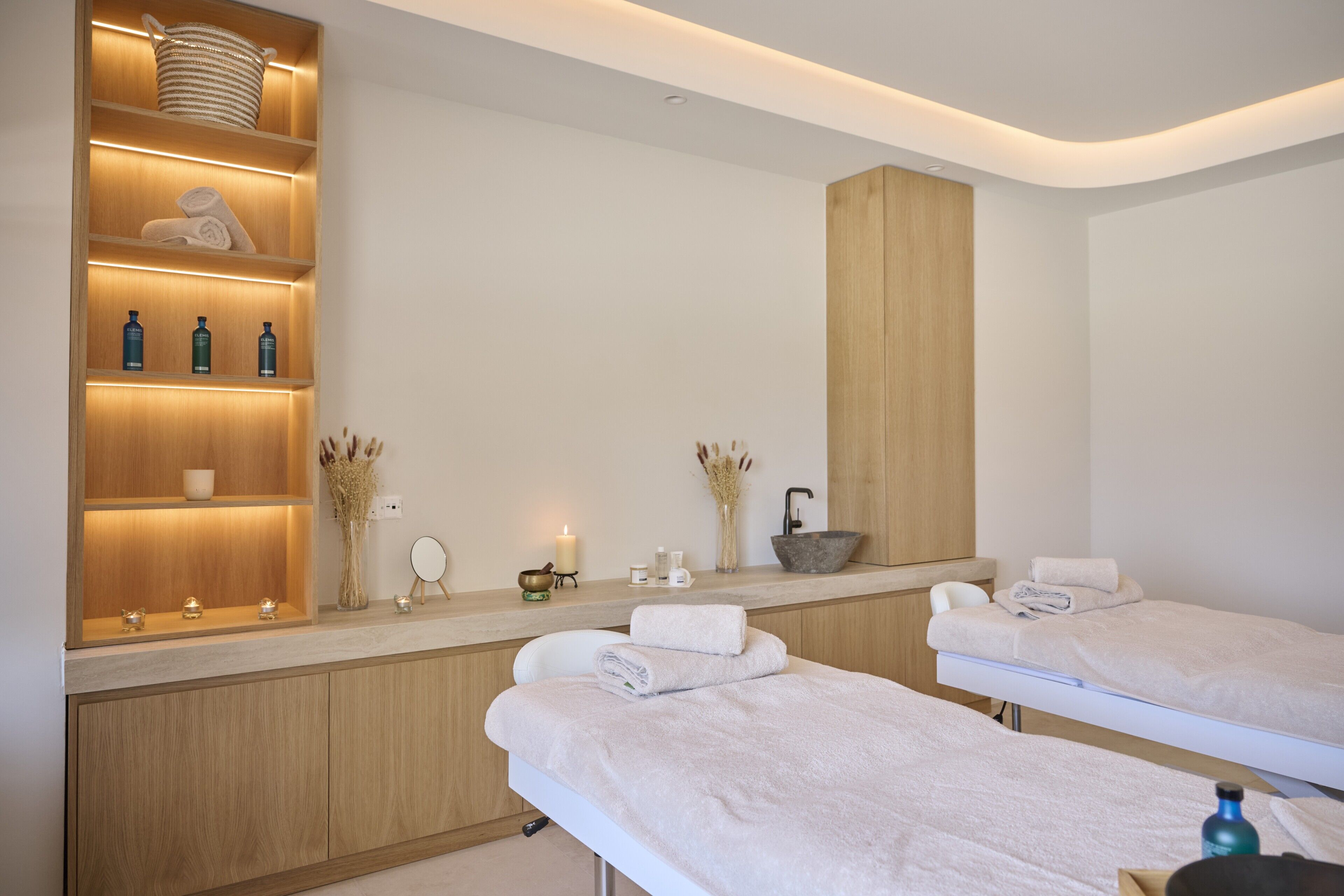 Un moderno spa con armarios de madera, un espejo grande, dos camillas y una encimera con diversos servicios.