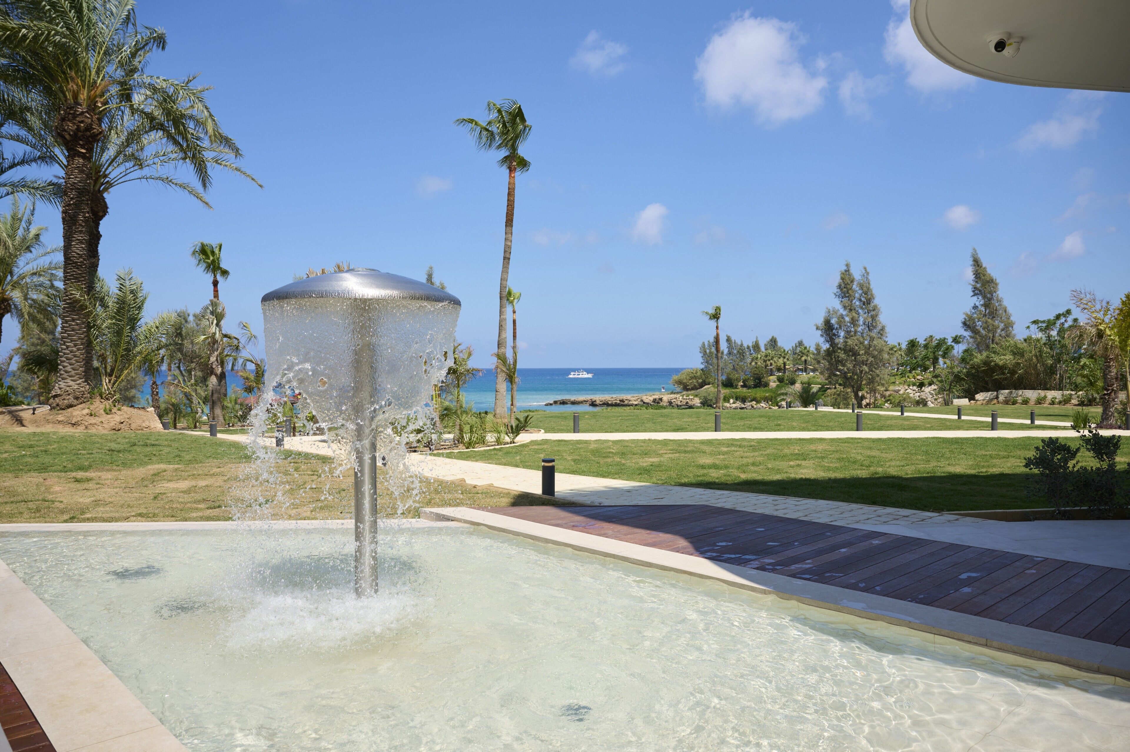 A pool with a water feature, palm trees, and a view of the ocean.