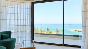 Ein Zimmer mit einer großen Schiebeglaswand, die auf einen Balkon mit Meerblick und einem entfernten Boot führt.