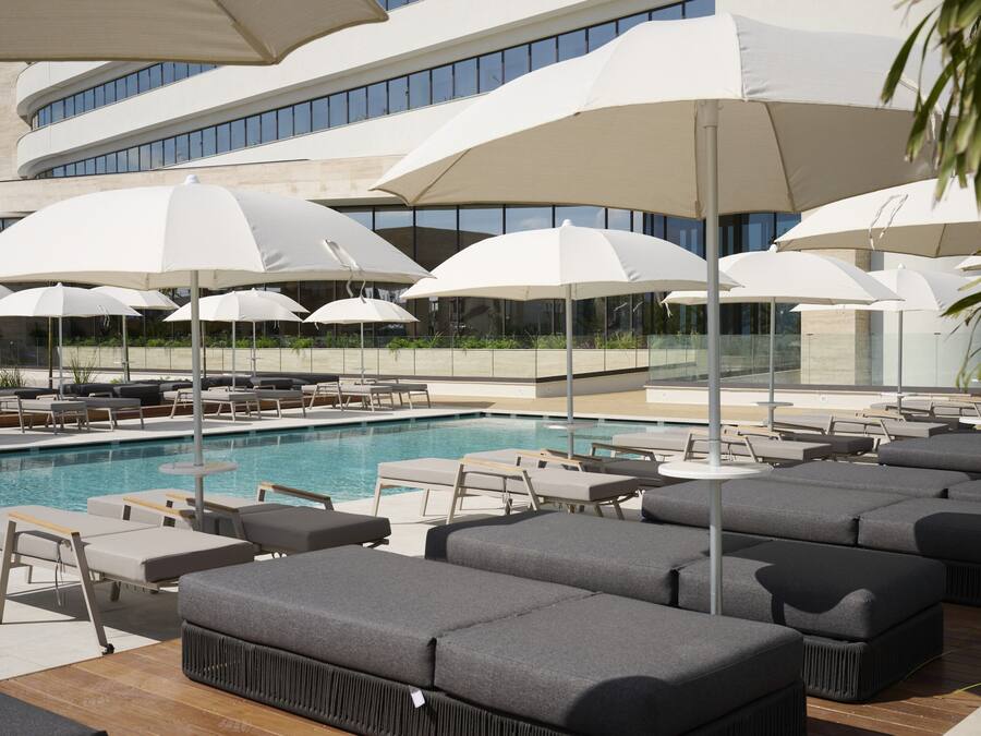 Un espace aménagé au bord de la piscine, avec des chaises longues et des parasols, une piscine et un bâtiment moderne en arrière-plan.