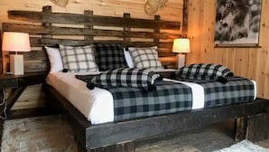 Ein Schlafzimmer mit Holzboden, einem Bett, zwei Nachttischen und einer Wandlampe.