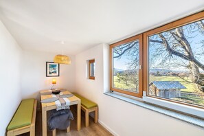 A room with a wooden table, bench, and a large window with a view of a tree and landscape.