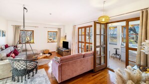 A spacious living room with a sofa, a hanging chair, a television, and a large sliding glass door leading to a balcony.