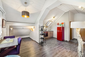 A loft-style room with a dining area, kitchen, and a large window.