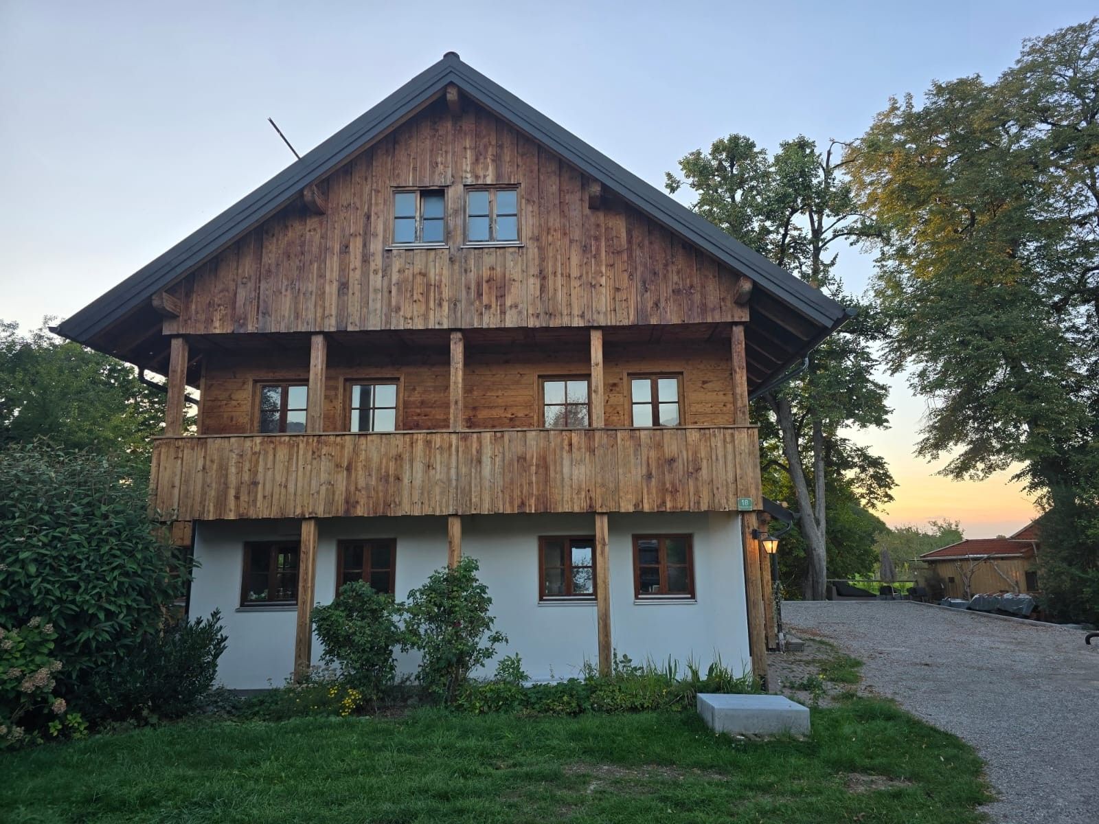 Une maison en bois à deux étages, dotée d’un balcon et entourée de verdure.
