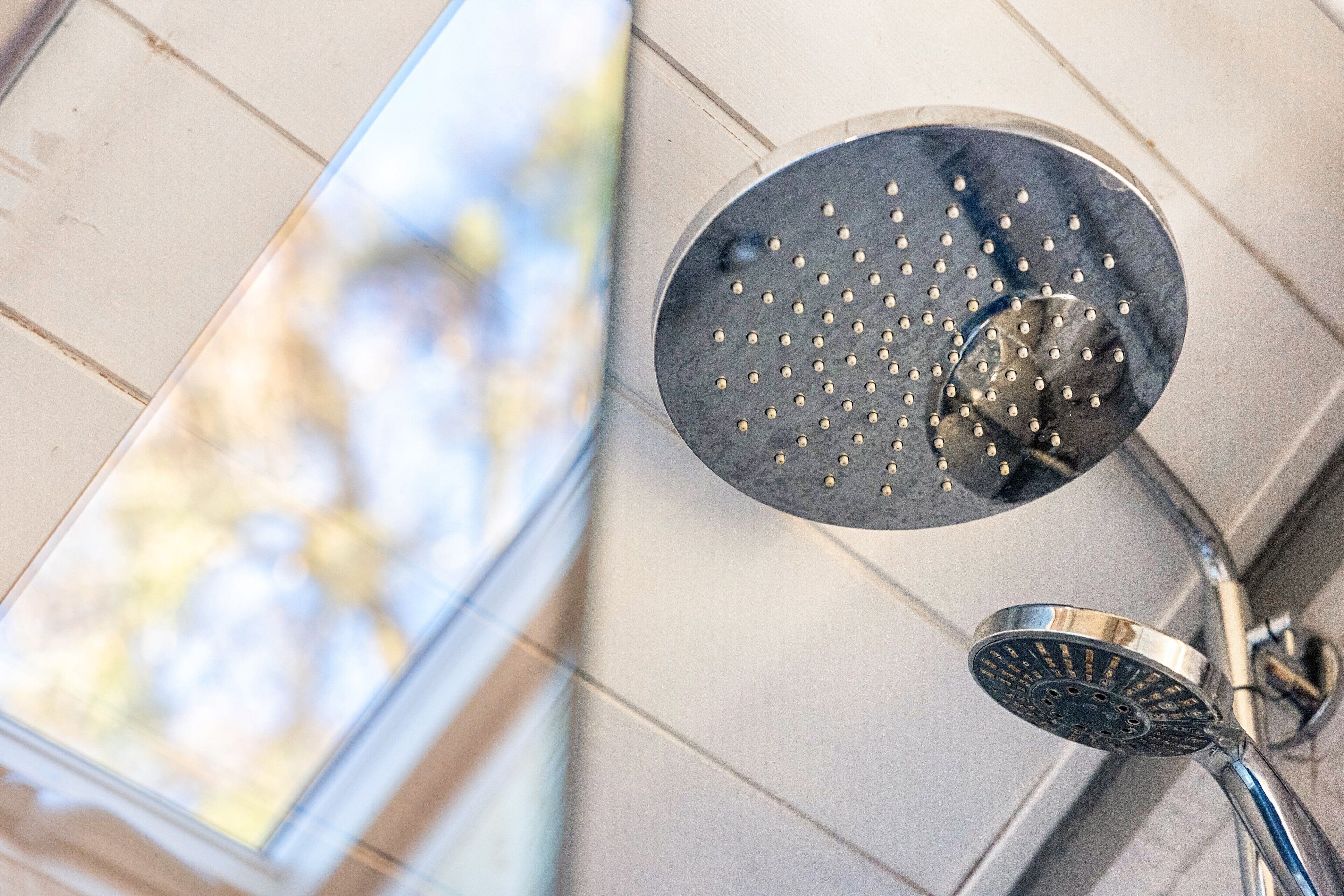 A showerhead with a circular design and multiple holes, mounted on a wall with a tiled surface.