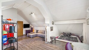 Un dormitorio estilo loft con techo inclinado, una cama con colcha estampada, un sofá, una mesita y un estante con diversos objetos.