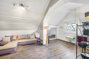 A loft-style room with a high ceiling, a sectional sofa, a small table, and a lamp.