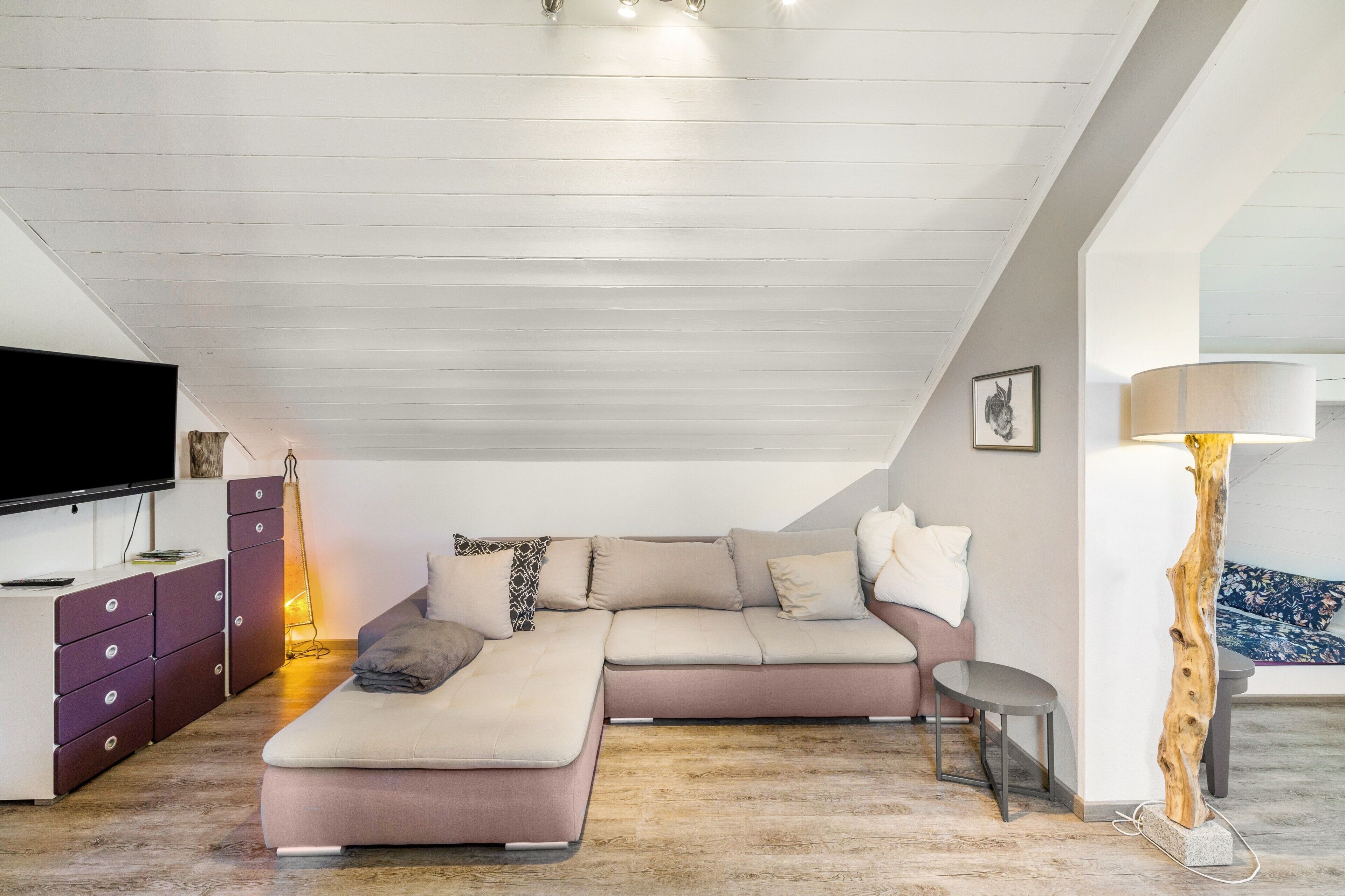 Ein modernes Wohnzimmer mit einem Ecksofa, einem Flachbildfernseher, Holzboden und einer außergewöhnlichen Leuchte.