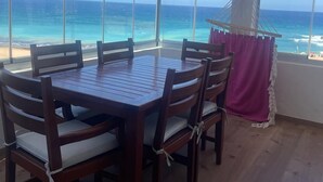 A wooden dining table with six chairs, large windows with a view of the ocean, and a beach visible through the windows. - atico azul (Tangier)