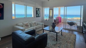 A spacious living room with a large window overlooking the sea, a white sofa, a black leather armchair, and a patterned rug. - atico azul (Tangier)