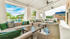 Un espace extérieur aménagé, abrité et doté de canapés, de fauteuils et d’une table, offrant une vue sur une piscine et un espace verdoyant.