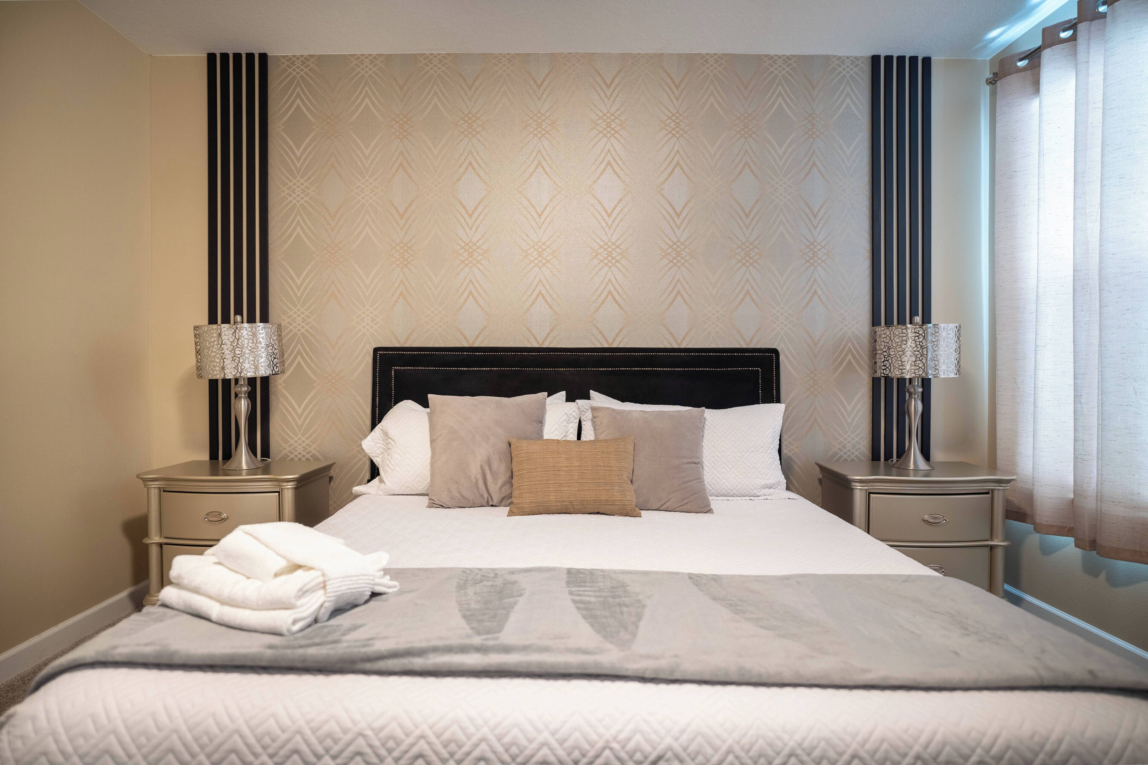 A neatly made bed with a patterned bedspread, two bedside lamps, and a folded towel on the nightstand.