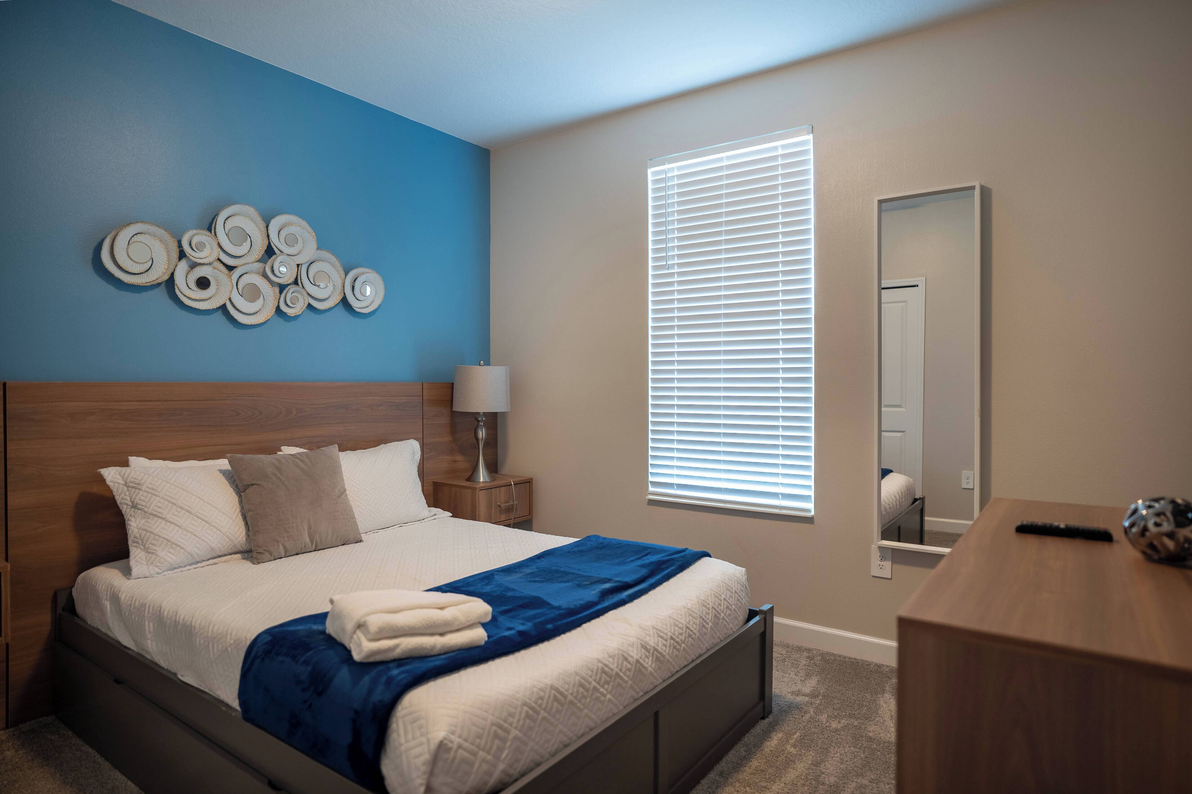 Un dormitorio con cama, mesita de noche, lámpara, espejo y cómoda.