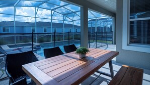 Een overdekt terras met een houten tafel, zwarte rieten stoelen en een potplant.