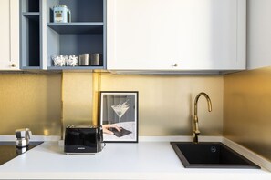 A modern kitchen with a black countertop, a framed picture of a martini glass, a toaster, and a gold-colored faucet. - Charming home near San Giovanni (Roma)