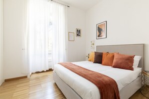 Un dormitorio ordenado con una cama grande, paredes blancas y suelo de madera.