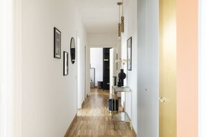 Un pasillo con suelo de madera, cuadros en las paredes, una puerta negra y una mesita con un florero.