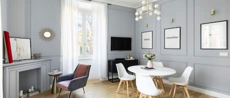 A modern living room with a fireplace, a dining area with a round table and white chairs, and a TV mounted on the wall.