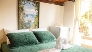 A bed with green bedding, white pillows, and a towel. There is a window with a view of greenery and a white wall with a framed picture. - Ref gio em Angra - Su te Vista Mar Pet Friendly (Angra dos Reis)