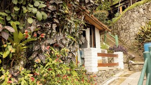 A rustic stone house with a wooden staircase leading to a white door, surrounded by lush greenery and a stone wall. - Ref gio em Angra - Su te Vista Mar Pet Friendly (Angra dos Reis)