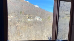 A room with a large window, a blue sofa, a wooden table, and a Spiderman pillow. - Apartment with Mountain View and Balcony (Saint-Colomban-des-Villards)