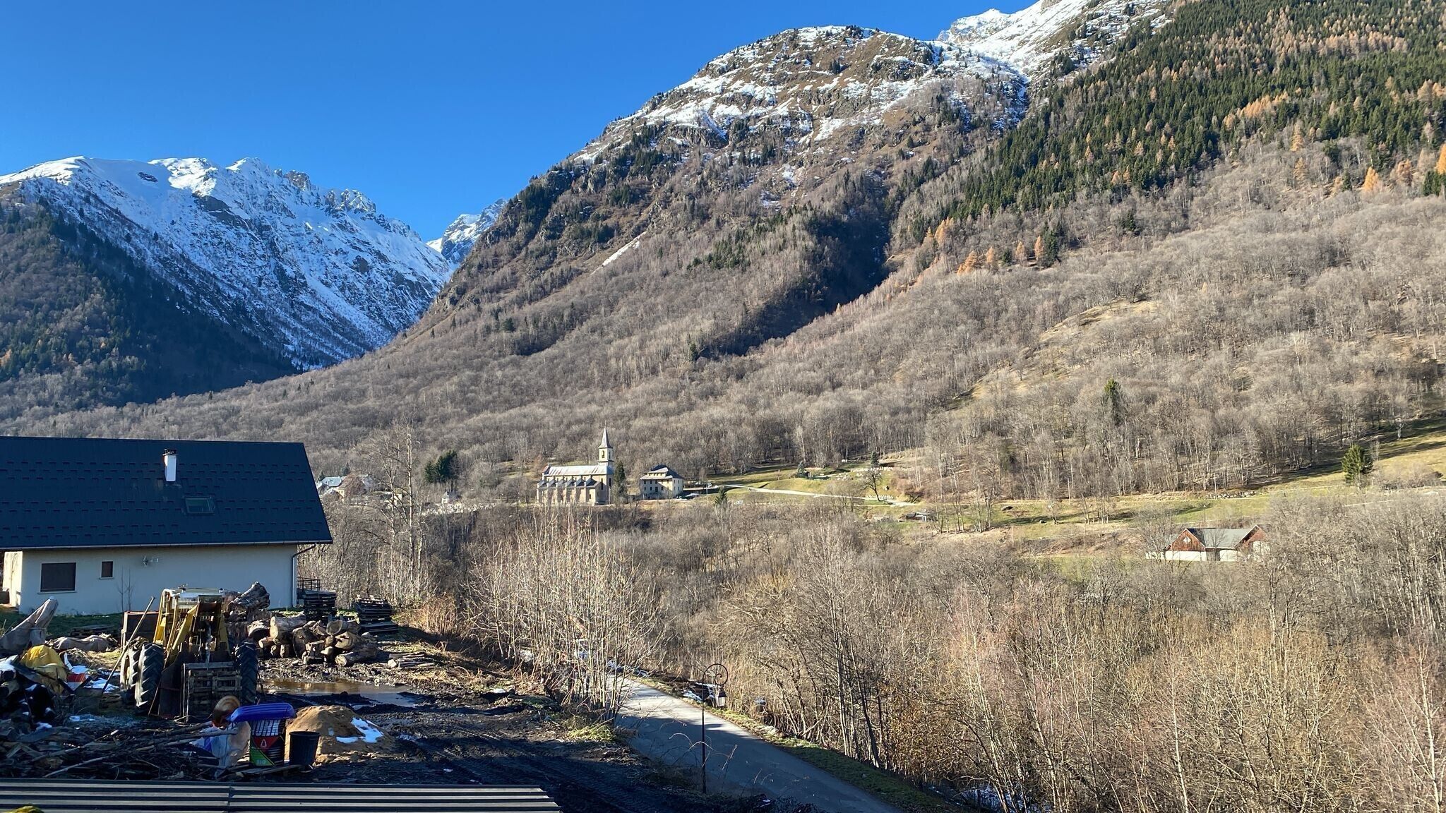 A mountainous landscape with a church, a building with a dark roof, and a road.