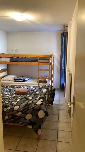 Habitación con literas, un edredón estampado, una mesita de noche y una cortina.