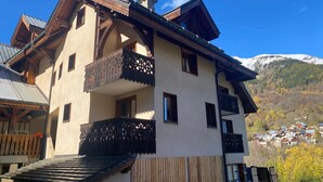 A multi-story building with balconies, a wooden facade, and a mountainous backdrop. - Apartment with Mountain View and Balcony (Saint-Colomban-des-Villards)