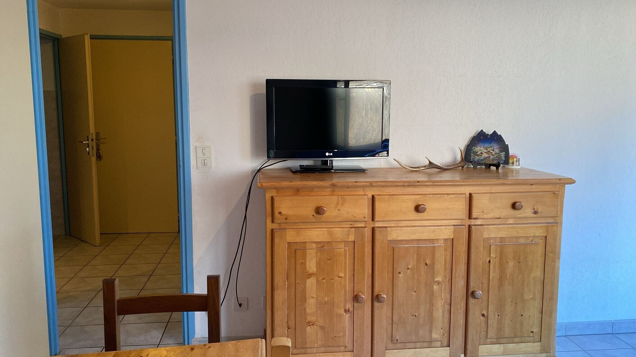 A wooden cabinet with a television on top, a small decorative item, and a door leading to another room.