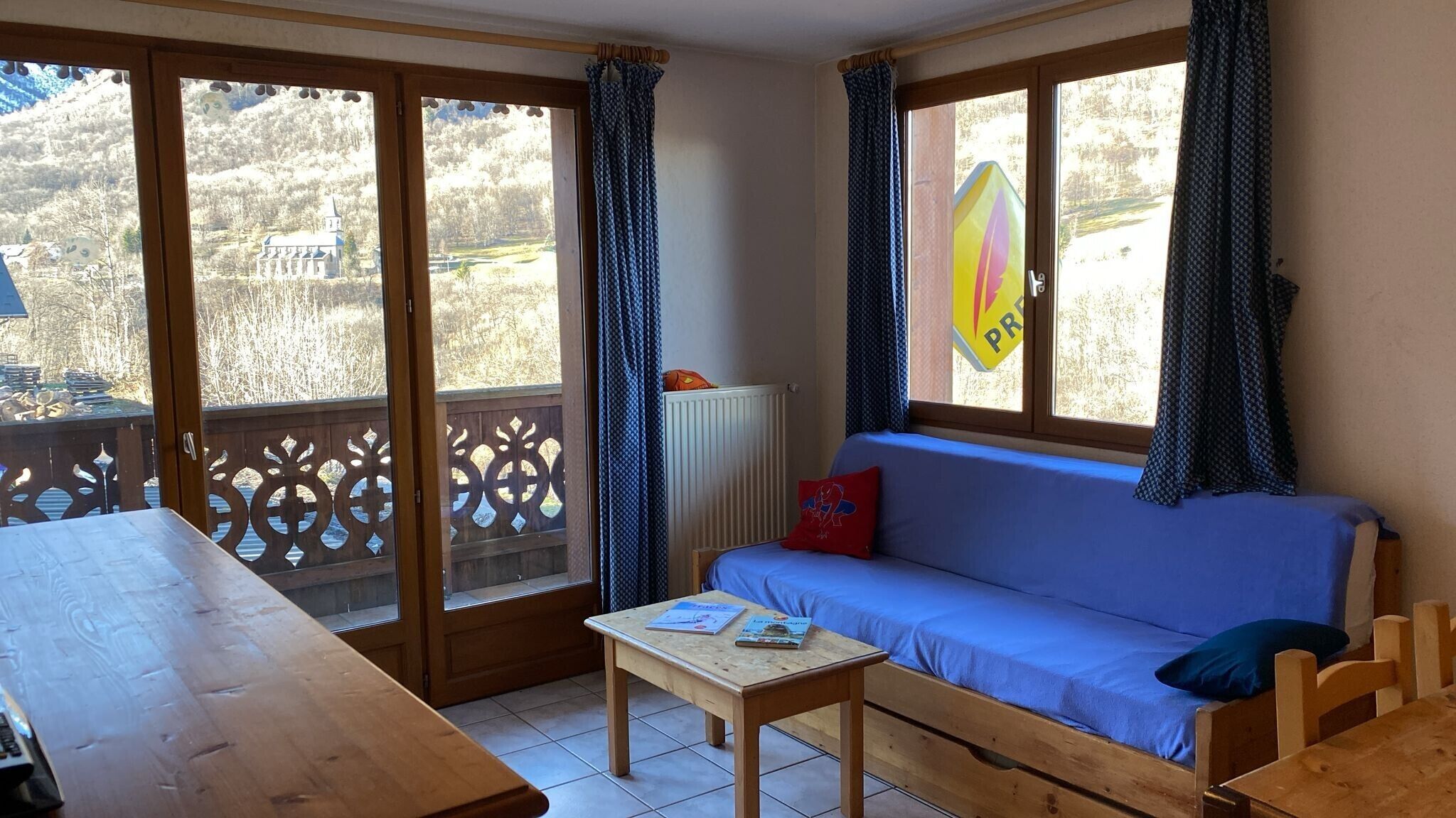 A room with a wooden table, a blue sofa, and a view of a mountain landscape through large windows.