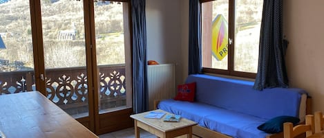 A room with a wooden table, a blue sofa, and a view of a mountain landscape through large windows.