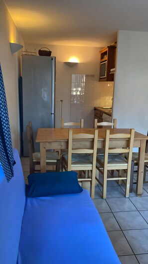 Una habitación con una cama, una mesa de comedor de madera con sillas, una zona de cocina y un radiador.