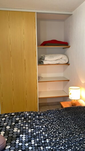 A bedroom with a wooden wardrobe, a bed with a black and white polka dot bedspread, a bedside lamp, and a shelf with folded clothes. - Apartment with Mountain View and Balcony (Saint-Colomban-des-Villards)