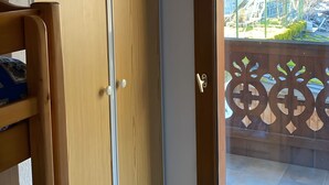 A room with a sliding wooden door, a wooden chair, and a glass door leading to an outdoor area with a view of a building and a fenced garden. - Apartment with Mountain View and Balcony (Saint-Colomban-des-Villards)