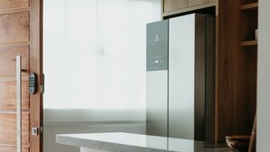 A modern kitchen with a built-in refrigerator, wooden cabinets, and a countertop. There are three stools and a large water dispenser. - Casa confortável estilo americana.Perto da praia e perto do centro. (Rio das ostras)