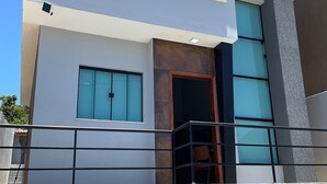 A modern two-story building with a balcony, large windows, and a flat roof. - Casa confortável estilo americana.Perto da praia e perto do centro. (Rio das ostras)