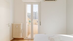 A bedroom with a bed, a radiator, a sliding glass door to a balcony, and a view of buildings. - GuestHost - A comfortable and welcoming 50 square meters apartment, perfect for four people, located on the eighth floor of a building (NO elevator).The property is located in the Washington neighborhood, a lively and well-equipped area of ​​Milan fi (Milan)
