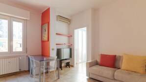 A living room with a sofa, a TV, a dining table with chairs, and a radiator. - GuestHost - A comfortable and welcoming 50 square meters apartment, perfect for four people, located on the eighth floor of a building (NO elevator).The property is located in the Washington neighborhood, a lively and well-equipped area of ​​Milan fi (Milan)