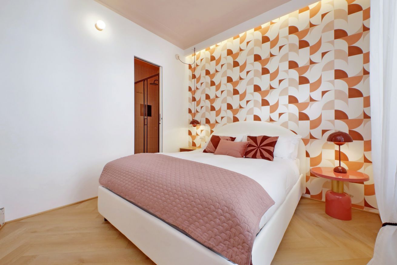 Une chambre à coucher moderne avec un grand lit, un mur orné d’un motif et une petite table de chevet avec une lampe.