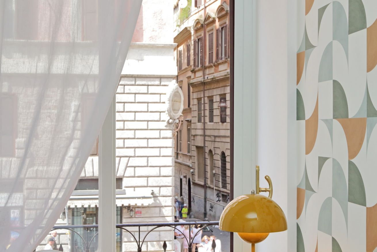A view from a balcony with a patterned wall, a street with buildings, and a yellow lamp.