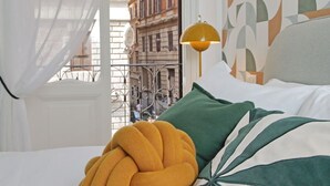 Una cama con una colcha amarilla, un almohadón verde y un muro con estampado geométrico.