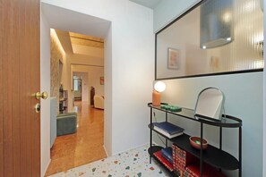 A hallway with a wooden door, a black metal shelf with books and a candle, and a mirror on the wall. - Colorful and classy apartment near Fori Imperiali (Roma)