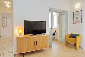 A modern living room with a wooden cabinet, a flat-screen TV, a small lamp, and a yellow chair. - Colorful and classy apartment near Fori Imperiali (Roma)