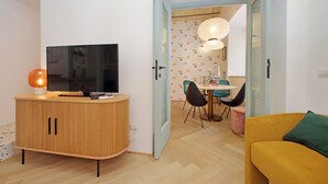 Una sala de estar moderna con un mueble de madera, un televisor de pantalla plana, un sofá amarillo y una zona de comedor con mesa y sillas.