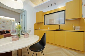 A modern kitchen with yellow cabinets, a large window, and a round dining table with black chairs. - Colorful and classy apartment near Fori Imperiali (Roma)